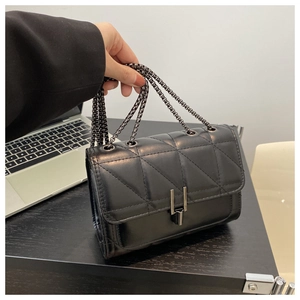 Detail of black quilted leather shoulder bag with dark metal chain and double bar clasp