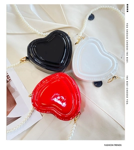 Detalle de bolsos de charol en forma de corazón negro, blanco y rojo con asa de perlas