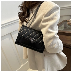 Close-up of black quilted shoulder bag featuring metal chain strap and geometric lock detail