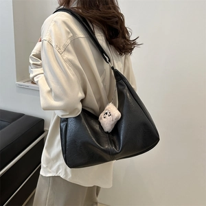 Minimalist black faux leather hobo bag with teddy charm shown on a model's shoulder