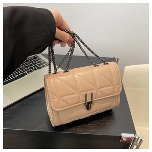 Detailed view of beige quilted cross-body bag featuring a dark grey metal clasp and chain strap