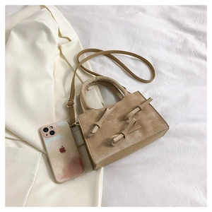 Detail of khaki bow handbag placed on white fabric with a phone for size scale