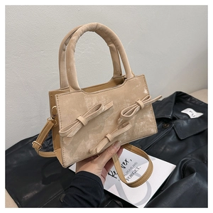 Close-up of beige crossbody bag featuring three decorative bows and round handle detail