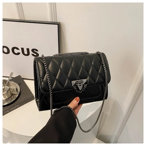 Detail of black quilted crossbody bag featuring metal chain strap and lock on white desk