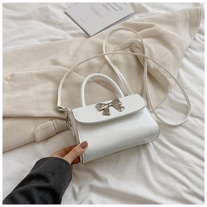 Detail of white square handbag with silver metal bow and polished faux leather texture