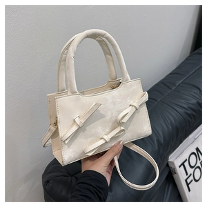Detail of cream white handbag with decorative bows and semi-circular handle