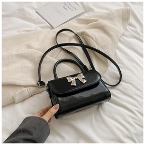 Detailed view of black patent leather mini handbag featuring a silver metal bow accent