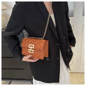 Close-up of brown quilted faux leather bag with gold H-clasp and chain on a black blazer