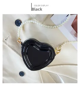 Detalle de bolso lacado negro de corazón con correa de perlas blancas falsas