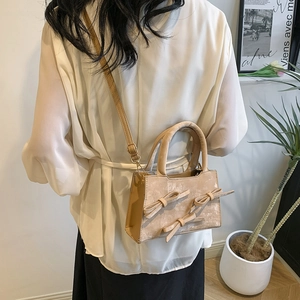 Beige crossbody bag with decorative bows and round handles shown on a model