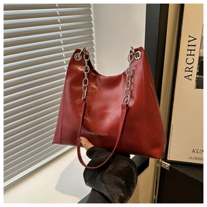 Dettaglio borsa a spalla in pelle bordeaux lucida con logo oro e tracolla a catena