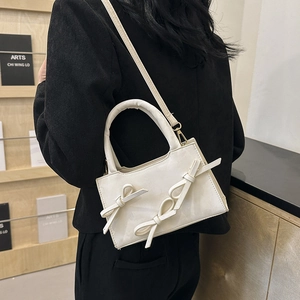 Chic cream-colored bow crossbody bag shown on a model against a warm library backdrop