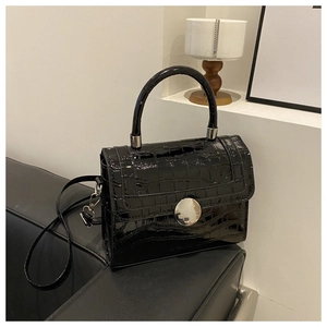 Detailed view of crocodile embossed leather and silver round lock on a black crossbody bag