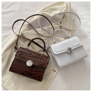 Detail of mini crocodile embossed handbags in brown and beige with round metal buckles