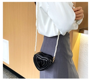Detalle de bolso lacado negro en forma de corazón con correa de perlas de lujo