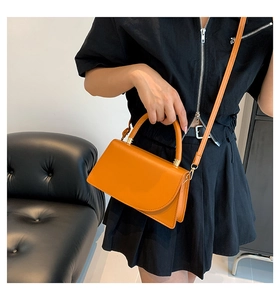 Detail of bright orange PU leather crossbody bag with golden metal hardware and top handle