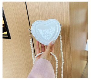 Detalle de bolso lacado blanco en forma de corazón con elegante cadena de perlas blancas