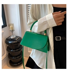 Detail of emerald green leather square crossbody bag with gold hardware and handle