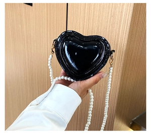 Vista detallada del bolso de corazón en charol negro con correa de perlas y broche dorado