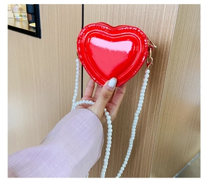 Detalle del bolso rojo con forma de corazón en charol brillante y correa de perlas finas