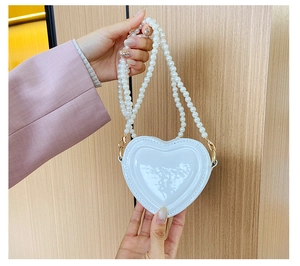 Detalle del bolso blanco con forma de corazón de charol con correa de perlas y acabado brillo