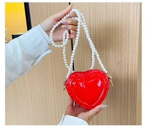 Detalle del mini bolso de corazón rojo en charol con correa de perlas blancas brillantes