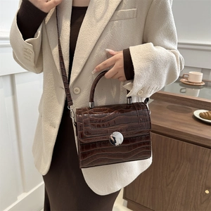 Brown crocodile pattern crossbody bag with silver circular lock in a lifestyle setting
