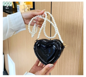 Detalle del bolso negro brillante en forma de corazón con correa de perlas artificiales