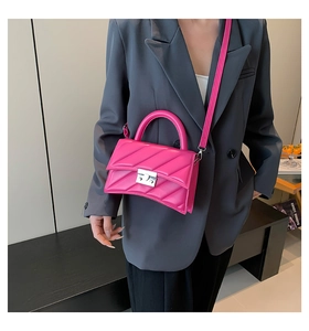 Détail d'un sac bandoulière matelassé fuchsia avec fermoir argenté sur un blazer