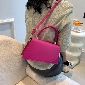 Chic rose red square crossbody bag with round handle and gold hardware on green knitwear