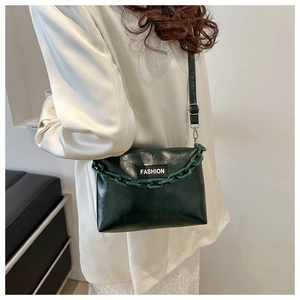Detail of dark green glossy leather bag with chunky chain and fashion label on white shirt