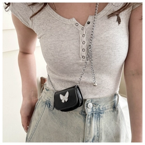 Detail of a mini black crossbody bag featuring a white pearlescent butterfly and silver chain
