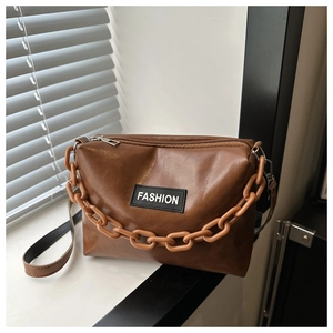Detail of dark brown leather crossbody bag with thick chain and fashion label on front