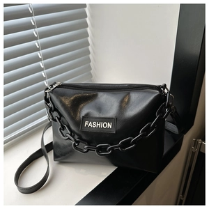 Close-up of black glossy leather crossbody bag with bold chain and FASHION label