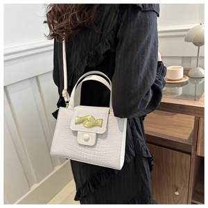 Détail d'un sac à main blanc à texture crocodile avec boucle dorée et bandoulière