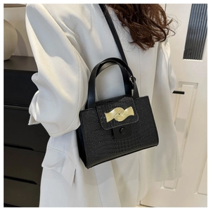 Détail du sac à main noir texture crocodile avec boucle dorée sur un manteau blanc