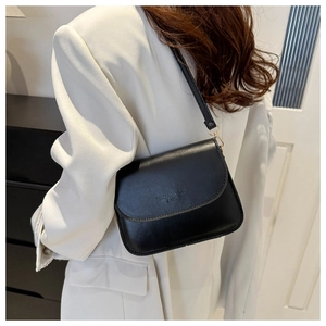 Detail of a minimalist black leather crossbody bag on a model wearing a white suit