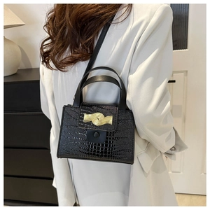 Détail du sac à main noir texture crocodile avec boucle dorée sur un blazer blanc
