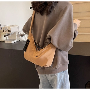 Detail of camel hobo bag with black dual zippers and decorative knots in a cafe setting