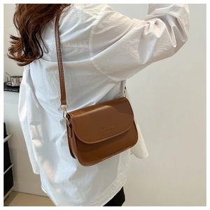 Detail of retro brown crossbody bag with flap closure and golden metal hook on model