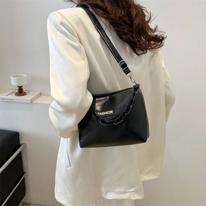 Modern black glossy leather hobo bag with thick chain and fashion label on a white blazer