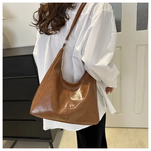 Side view of large brown caramel hobo bag in polished faux leather worn by a model