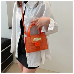 Détail du sac à main orange motif crocodile avec garniture dorée porté par un mannequin