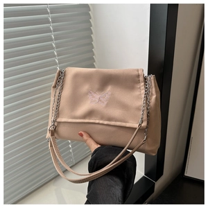 Close-up of pink butterfly embroidery and metallic chain on beige crossbody bag