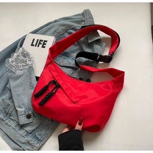 Detail of red crescent nylon bag featuring black wide strap and plastic buckle closure