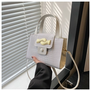 Détail d'un sac à main blanc motif crocodile avec boucle dorée ondulée et poignée