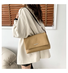 Detail of khaki pebbled leather flap bag featuring silver metal trim and striped wide strap