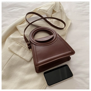 Detail of dark brown leather handbag with round handle and adjustable shoulder strap