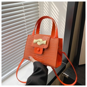 Détail d'un sac à main orange motif crocodile avec boucle en métal doré ondulé gros plan