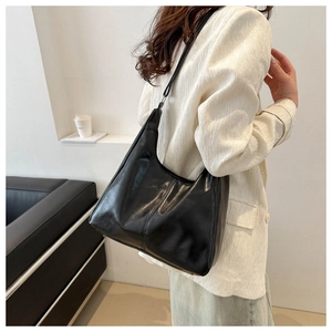 Detail view of a large black leather tote bag with vertical stitching on white suit